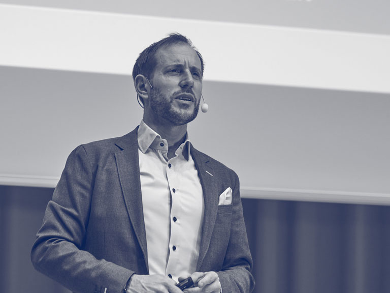 i kostym håller en presentation inför en publik.